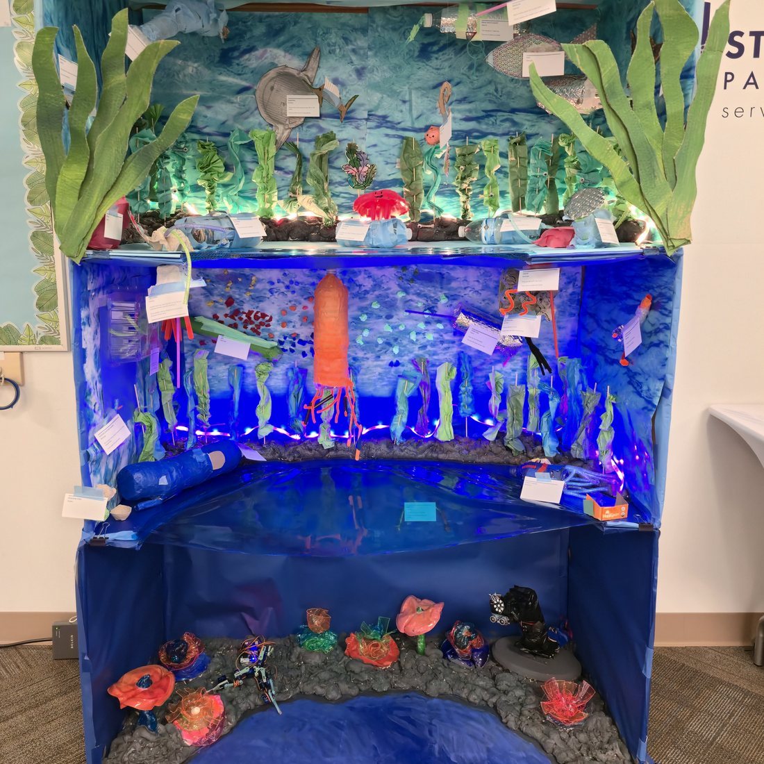 A three-level student-built ocean diorama with kelp, glowing jellyfish and LED lighting.